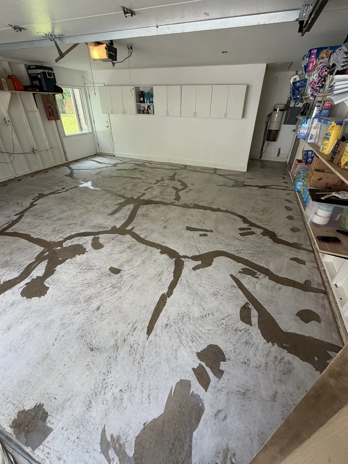 Garage floor before coating: bare concrete with dark stains, white cabinets on the back wall